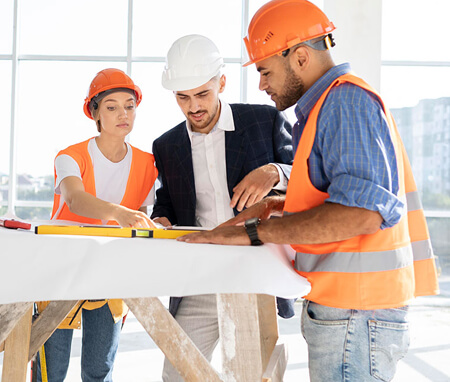 Three construction professionals reviewing plans at a building site.